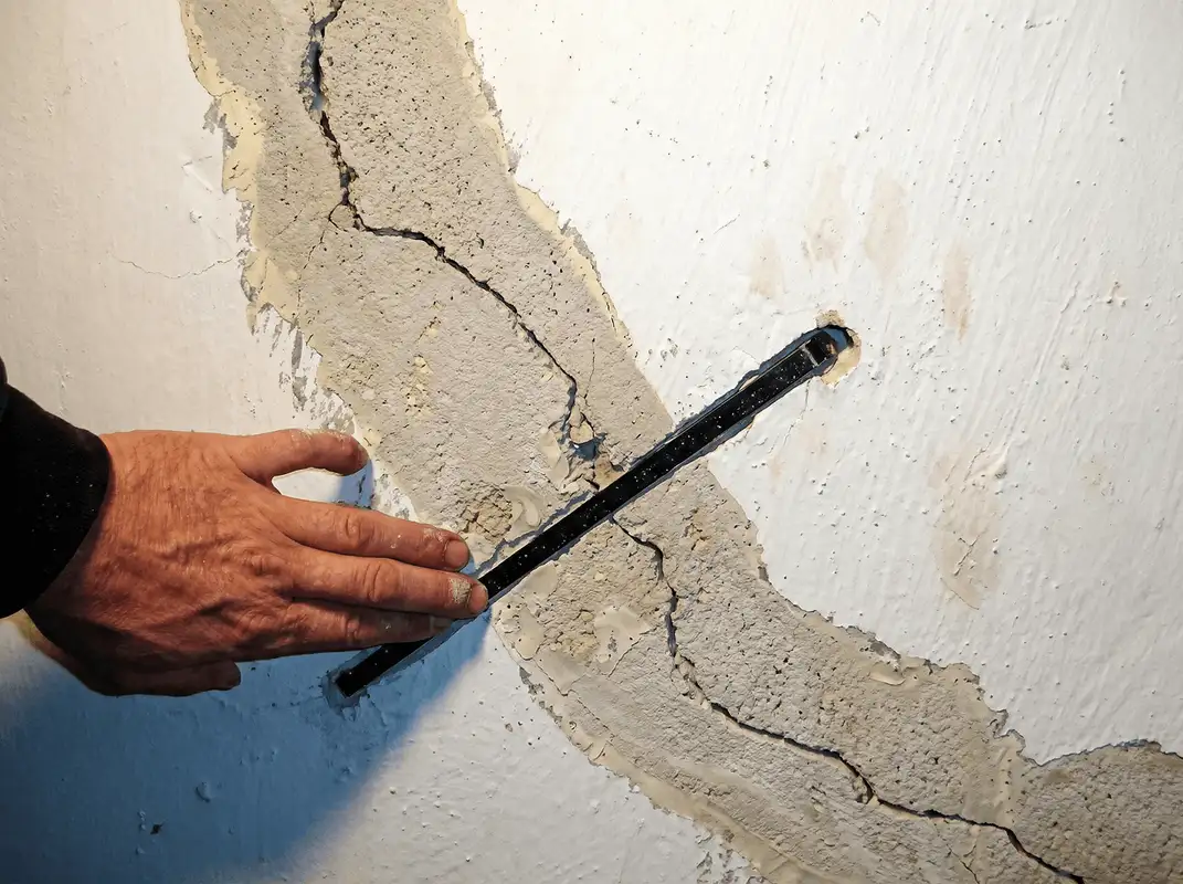 A wall with a large crack is being inspected by a professional in Baton Rouge, LA