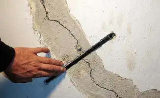 A wall with a large crack is being inspected by a professional in Baton Rouge, LA